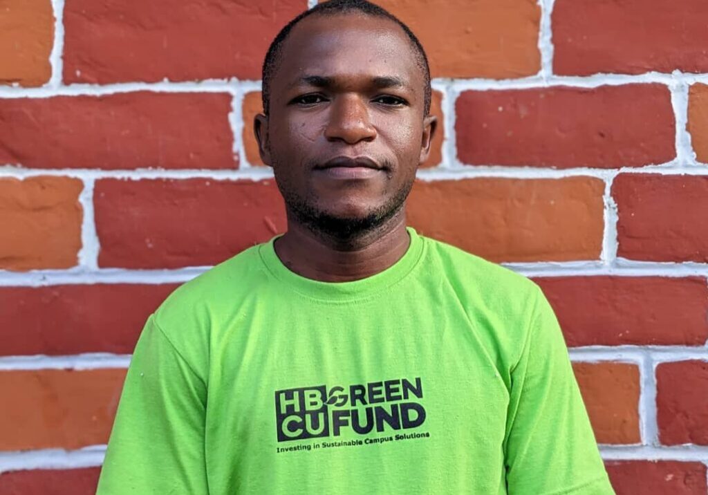 A man in a green shirt standing next to a brick wall.